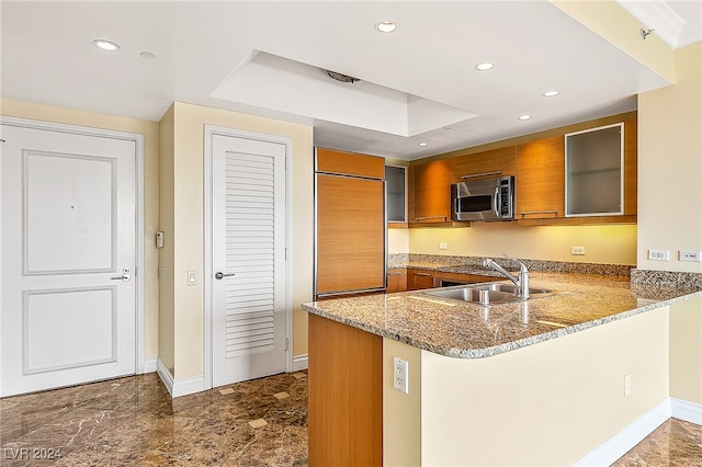 kitchen with kitchen peninsula, paneled refrigerator, light stone counters, and sink