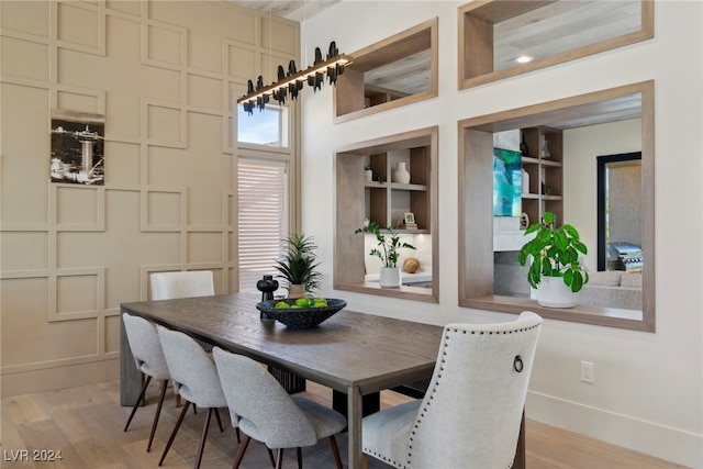 dining space with built in features, a towering ceiling, and light hardwood / wood-style floors