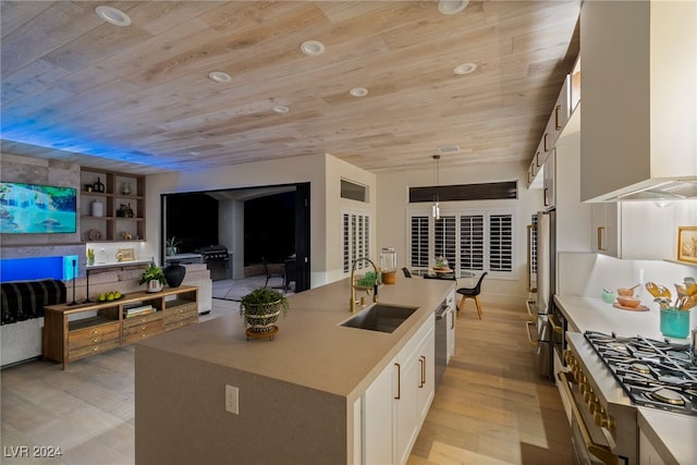 kitchen with light wood-type flooring, a kitchen island with sink, sink, wall chimney range hood, and white cabinets