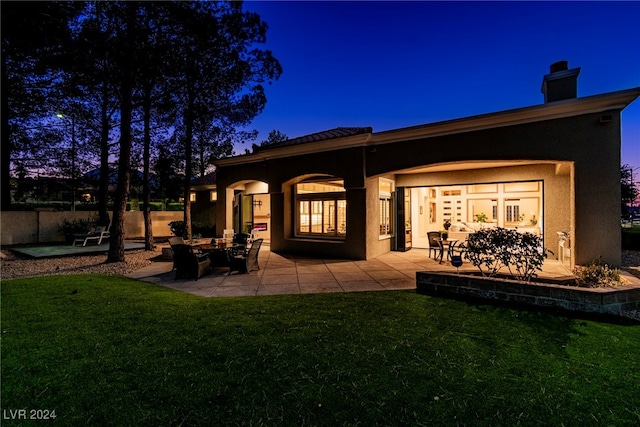 back house at dusk with a patio area and a yard