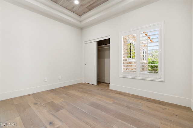 unfurnished bedroom with light hardwood / wood-style floors, a raised ceiling, wooden ceiling, and a closet