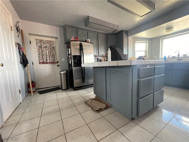 kitchen featuring sink, stainless steel fridge, a textured ceiling, gray cabinets, and light tile patterned floors