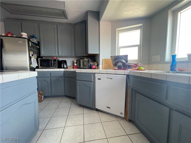 kitchen featuring appliances with stainless steel finishes, a textured ceiling, a wealth of natural light, and tile counters