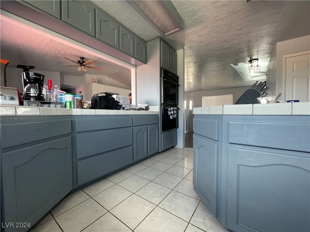 kitchen featuring tile countertops, ceiling fan, black double oven, and a textured ceiling