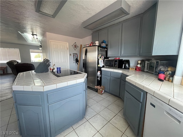 kitchen with a textured ceiling, stainless steel appliances, tile counters, and light tile patterned flooring