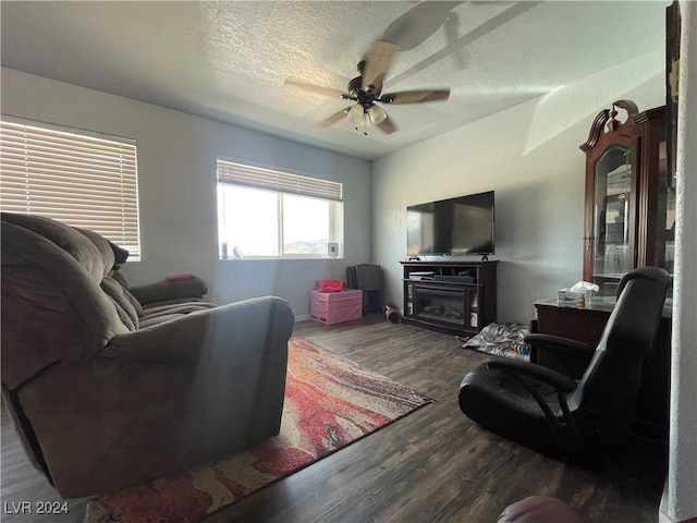 living room featuring ceiling fan, a fireplace, dark wood-type flooring, and a textured ceiling