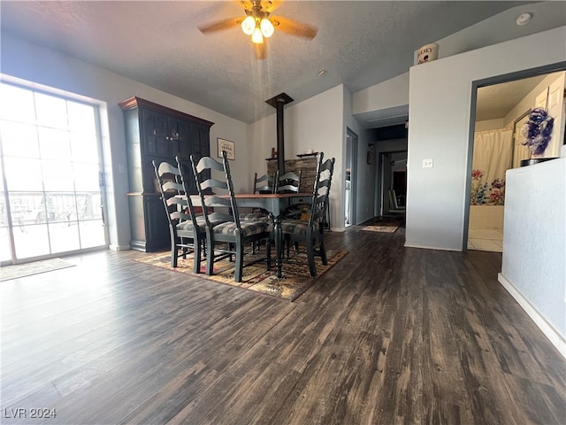 dining room featuring ceiling fan, a wood stove, a textured ceiling, and dark wood-type flooring