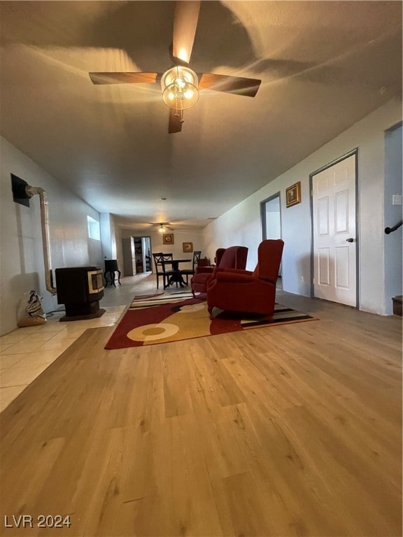 living room with light wood-type flooring, a wood stove, and ceiling fan