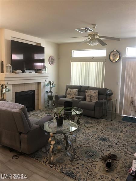 living room with a tile fireplace, wood-type flooring, and ceiling fan