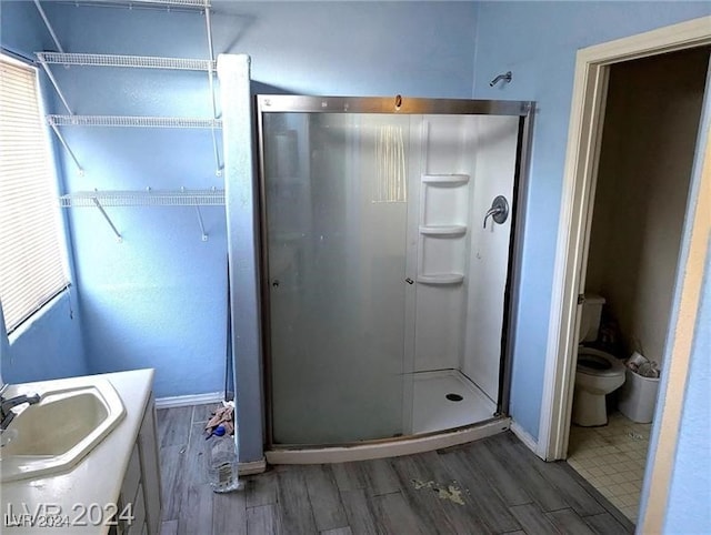 bathroom featuring a shower with door, vanity, hardwood / wood-style floors, and toilet