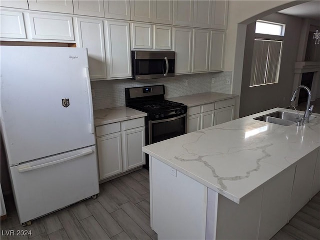 kitchen with white cabinetry, sink, black range oven, light stone countertops, and white refrigerator