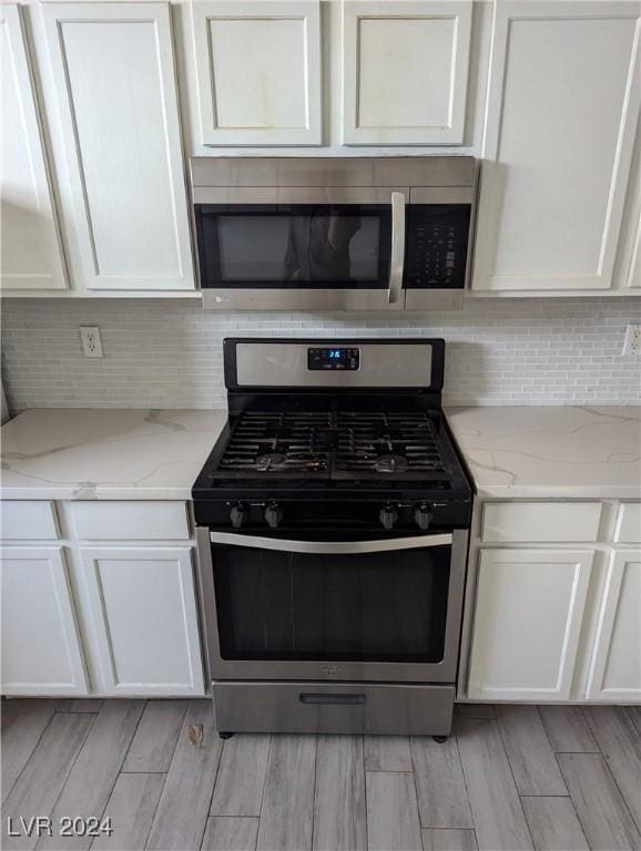 kitchen featuring light stone countertops, white cabinetry, light wood-type flooring, and appliances with stainless steel finishes