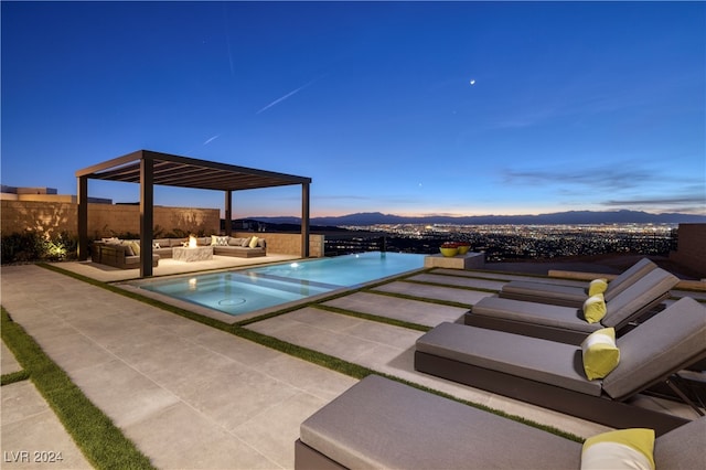 pool at dusk featuring a mountain view, an in ground hot tub, an outdoor hangout area, and a patio