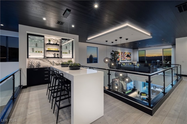 kitchen with pendant lighting, a kitchen breakfast bar, black cooktop, a large island, and light hardwood / wood-style floors