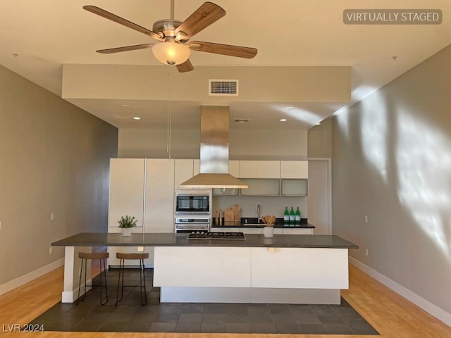 kitchen featuring black microwave, white cabinetry, stainless steel oven, a breakfast bar area, and island range hood