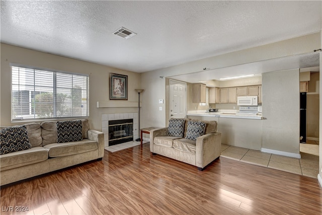 living room with a tile fireplace, a textured ceiling, and light hardwood / wood-style flooring