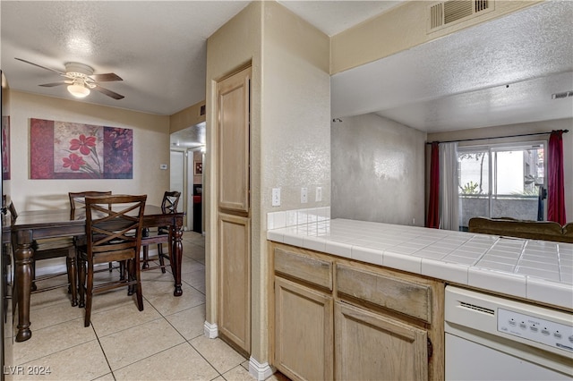 kitchen featuring ceiling fan, tile countertops, white dishwasher, a textured ceiling, and light tile patterned floors