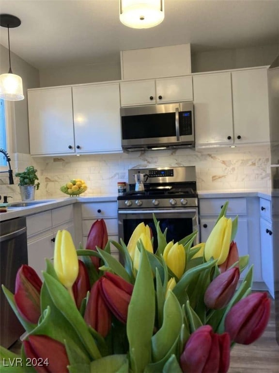 kitchen featuring appliances with stainless steel finishes, backsplash, hardwood / wood-style flooring, decorative light fixtures, and white cabinets