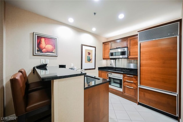145 Harmon Ave Unit 208, Las Vegas, NV 89109 - kitchen with appliances with stainless steel finishes, a peninsula, dark countertops, brown cabinetry, and light tile patterned flooring