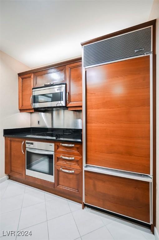 145 Harmon Ave Unit 208, Las Vegas, NV 89109 - kitchen featuring appliances with stainless steel finishes, dark countertops, brown cabinetry, and light tile patterned floors