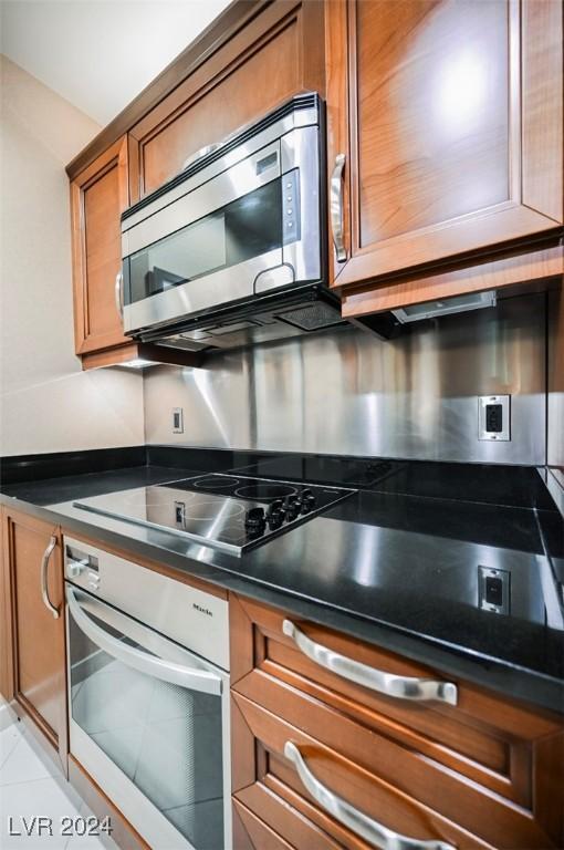 145 Harmon Ave Unit 208, Las Vegas, NV 89109 - kitchen featuring oven, stainless steel microwave, brown cabinetry, dark countertops, and black electric stovetop