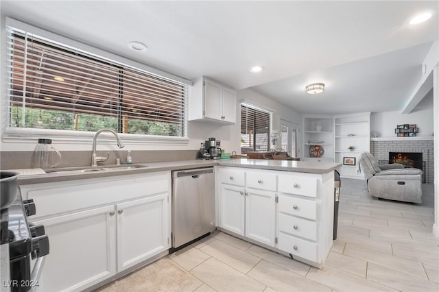 kitchen featuring dishwasher, a brick fireplace, white cabinetry, and sink