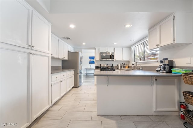 kitchen featuring kitchen peninsula, appliances with stainless steel finishes, sink, white cabinetry, and a breakfast bar area