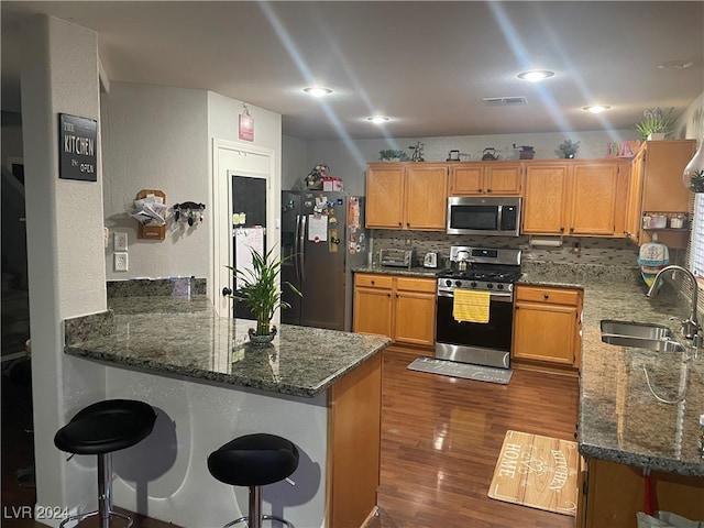 kitchen with sink, stainless steel appliances, dark stone countertops, and kitchen peninsula