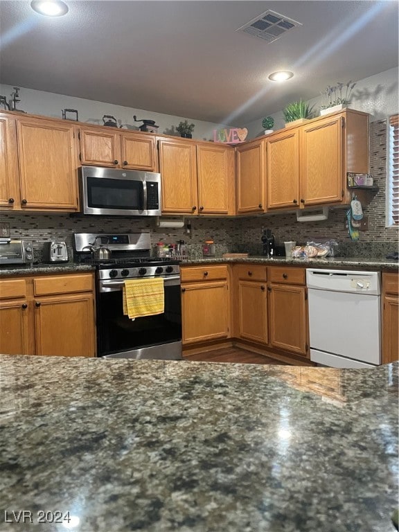 kitchen featuring appliances with stainless steel finishes, dark stone countertops, and decorative backsplash