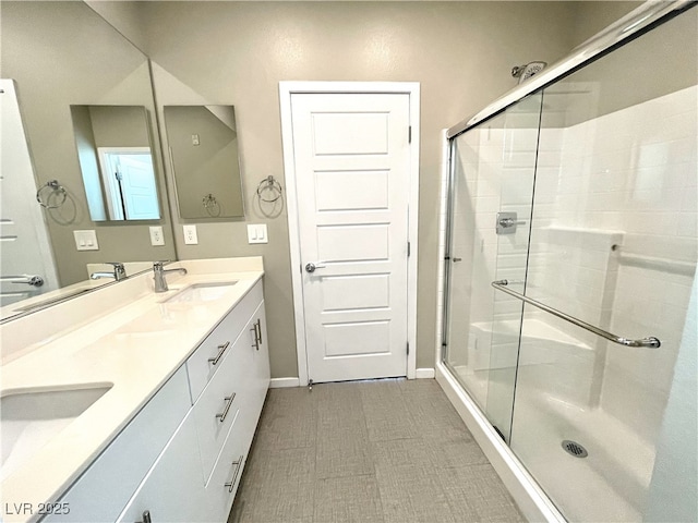 full bathroom with double vanity, a shower stall, baseboards, and a sink