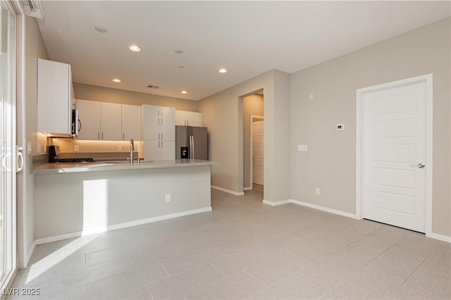 kitchen with range, sink, stainless steel fridge, white cabinetry, and kitchen peninsula