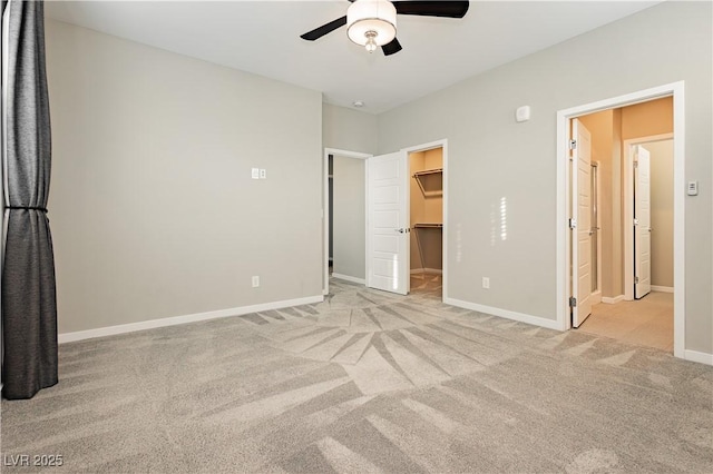 unfurnished bedroom with carpet floors, a walk in closet, a ceiling fan, and baseboards