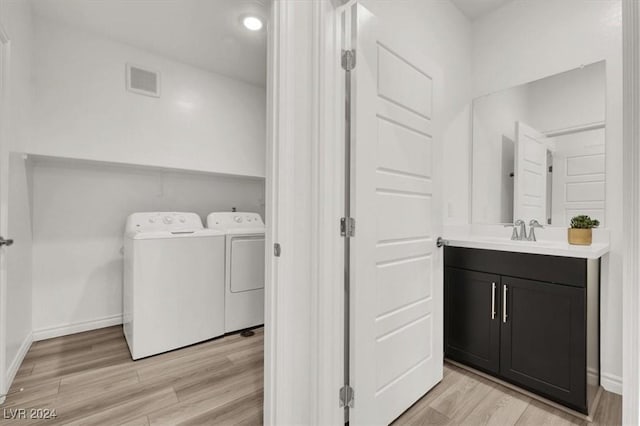 clothes washing area with separate washer and dryer, sink, and light wood-type flooring