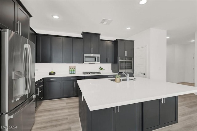 kitchen with sink, light wood-type flooring, stainless steel appliances, and a kitchen island with sink