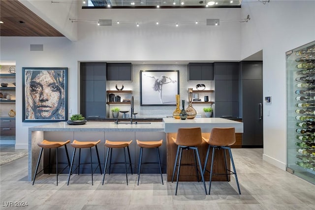 kitchen featuring sink, a large island with sink, a towering ceiling, a kitchen bar, and decorative backsplash