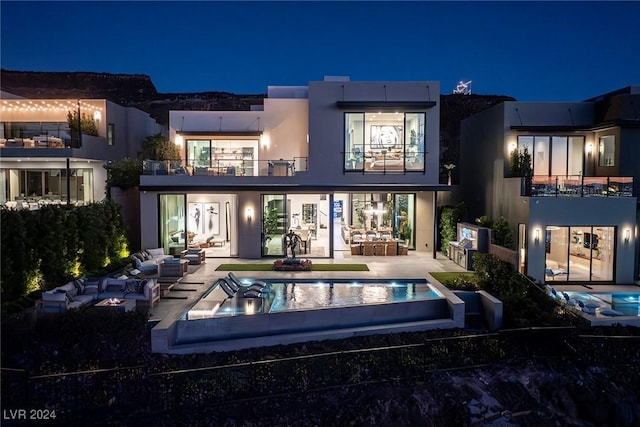 back house at night featuring outdoor lounge area, a balcony, and a patio