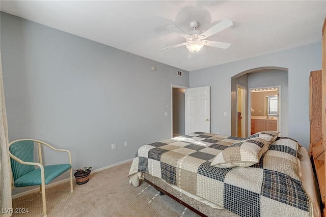 carpeted bedroom featuring arched walkways, connected bathroom, visible vents, a ceiling fan, and baseboards