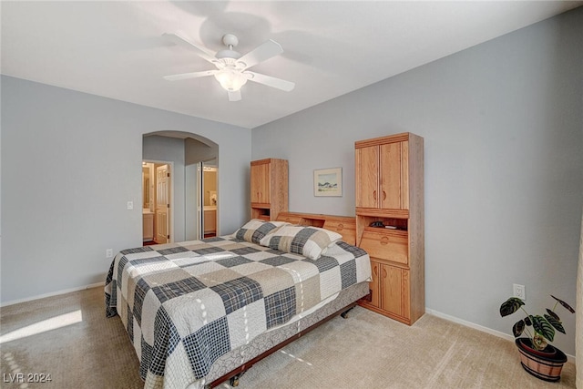 bedroom with arched walkways, light carpet, connected bathroom, ceiling fan, and baseboards