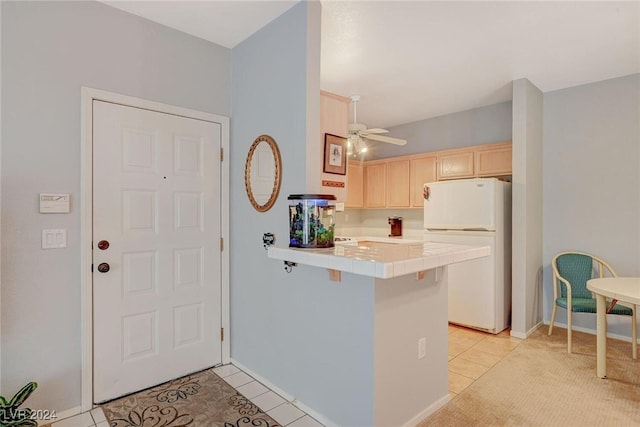 kitchen featuring light tile patterned floors, a peninsula, tile counters, freestanding refrigerator, and light brown cabinetry