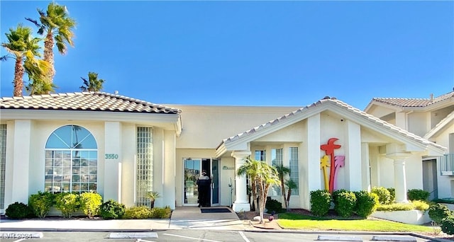 view of front of house with uncovered parking, a tile roof, and stucco siding