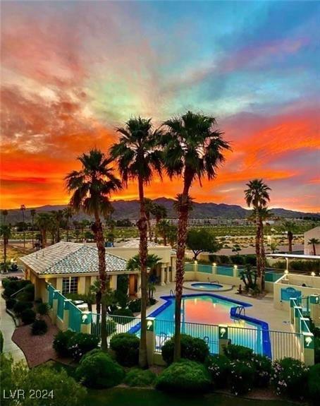 pool at dusk featuring a hot tub, a mountain view, and a patio area