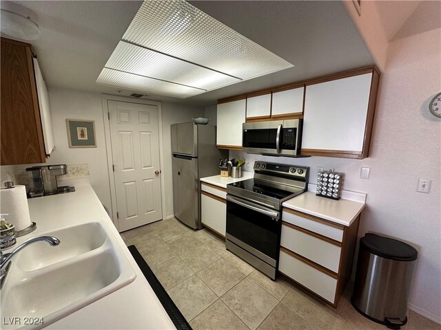 kitchen with white cabinetry, stainless steel appliances, a sink, and light countertops