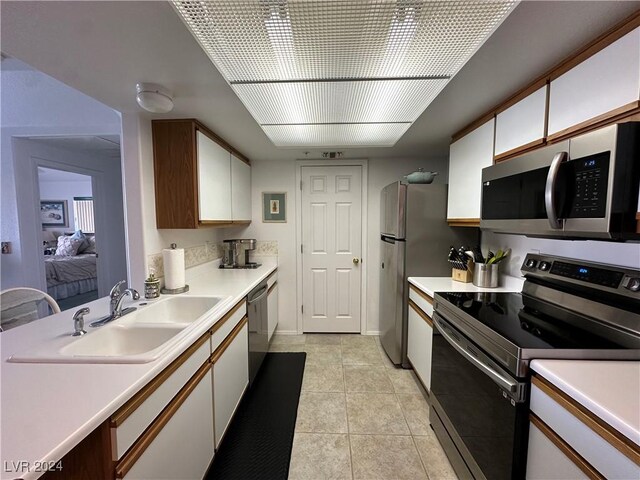 kitchen featuring light tile patterned floors, white cabinets, appliances with stainless steel finishes, light countertops, and a sink