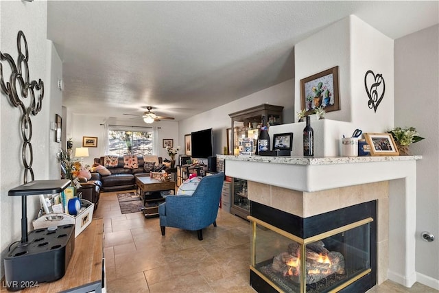 living room with tile patterned floors, ceiling fan, a textured ceiling, and a tile fireplace