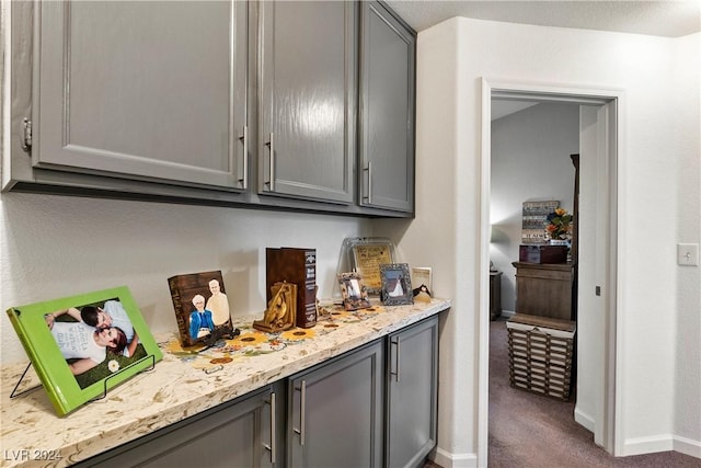 bar featuring gray cabinetry, dark carpet, and light stone countertops