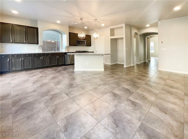 kitchen featuring appliances with stainless steel finishes, backsplash, dark brown cabinetry, pendant lighting, and a center island