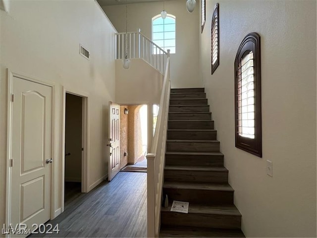 stairway with hardwood / wood-style floors and a towering ceiling