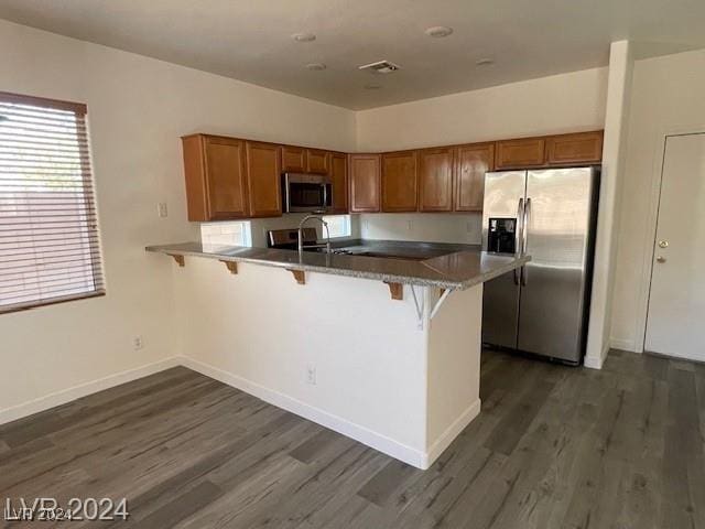 kitchen featuring kitchen peninsula, dark hardwood / wood-style flooring, a breakfast bar, stainless steel appliances, and sink