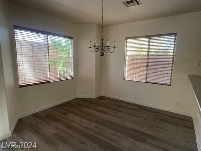 unfurnished dining area with a chandelier, plenty of natural light, and dark wood-type flooring