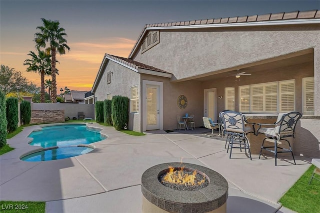 pool at dusk featuring ceiling fan, a patio, and an outdoor fire pit